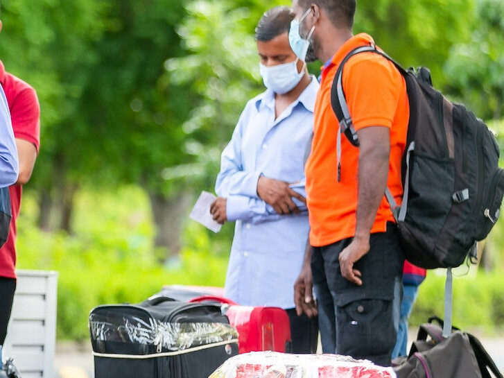 Auf dem Bild stehen zwei Männer mit Mundschutz, vor ihnen sind Koffer zu sehen.