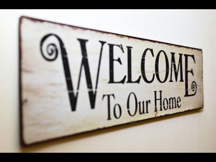 Ein Holzschild, das an der Wand hängt, mit der Aufschrift: "Welcome to our home".
