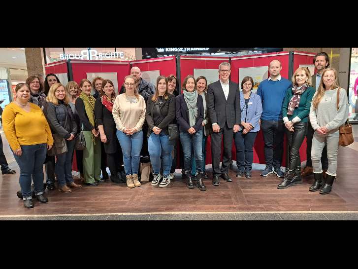 Die Veranstalterinnen und Veranstalter des Demenzquartals stehen im Einkaufszentrum Rhein-Neckar vor den roten Stellwänden, auf denen die Cartoons von Peter Gaymann unter dem Motto "Demensch" angebracht sind.