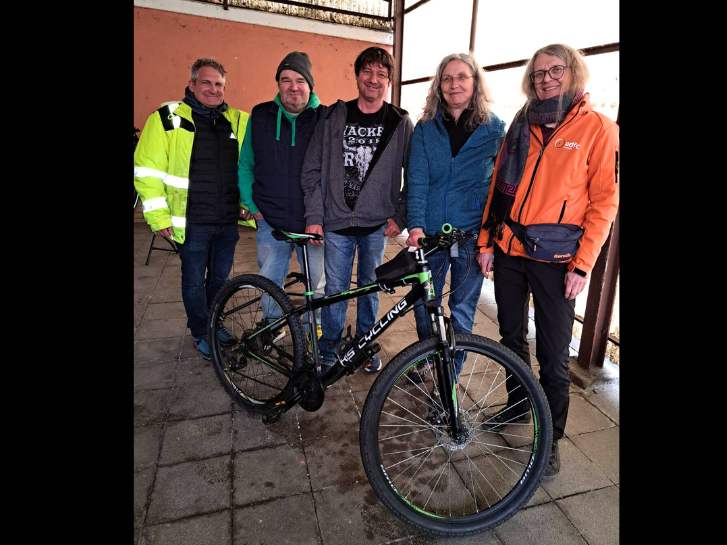 hinter einem frisch reparierten Fahrrad stehen 3 Männer und 2 Frauen.