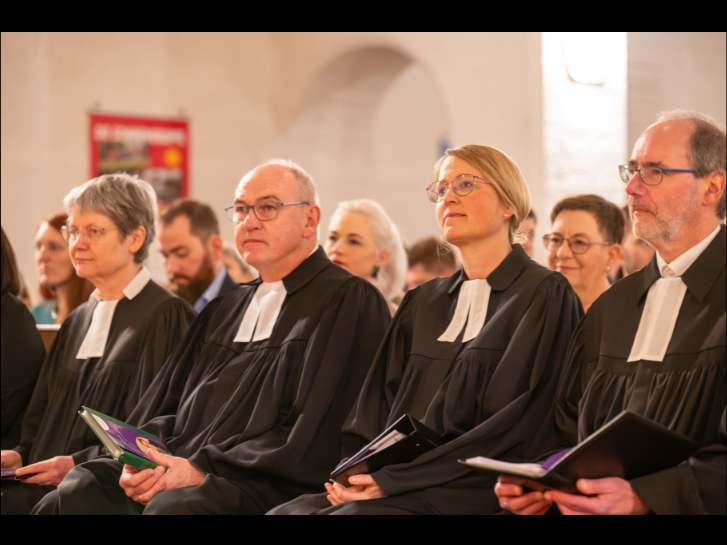 In einem Gottesdienst sitzen in einer Reihe v.l. die stellvertretende Dekanin Bienhaus, der scheidende Dekan Kreh, die Dekanin Mattes und Probst Arras. Alle tragen einen Talar.