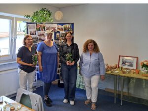 Die 2 Sozialpädagoginnen und die 2 Frauen der Hausleitung stehen neben dem Buffet und vor der Bilderwand im Psychosozialen Zentrum in Rimbach.