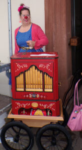 Clownin Rosa steht mit der Drehorgel am Ausgang der evangelischen Kirche Rimbach