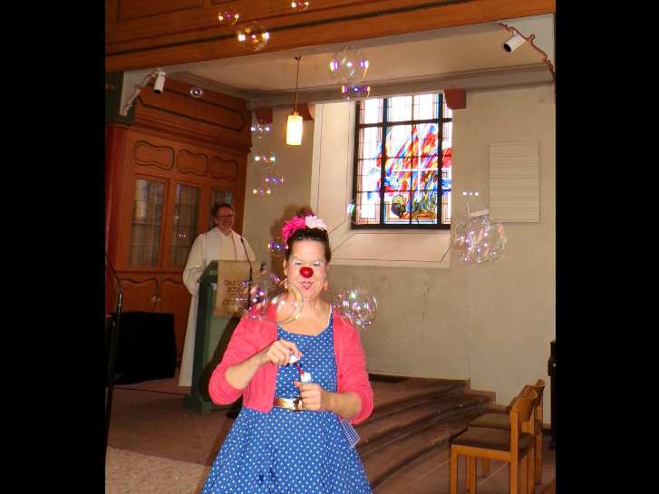 Clownin mit steht in der evangelischen Kirche in Rimbach. Sie ist von Seifenblasen umgeben. Im Hintergrund, am Rednerpult, steht Pfarrer Uwe Buß.