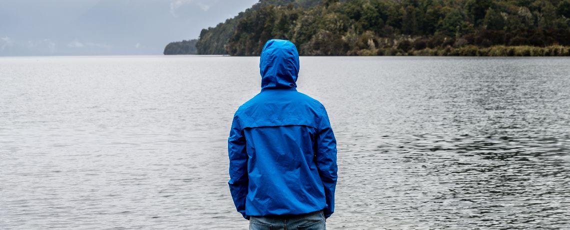 Bild von einer Person mit blauer Regenjacke, die auf einen See blickt.