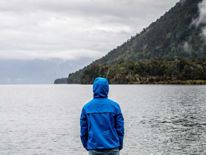 Foto von einer Person mit blauer Regenjacke, die auf einen See blickt.