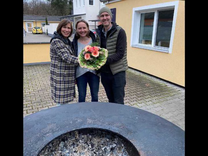 Björn und Sabine Terhorst stehen zusammen mit der Tafelkoordinatorin Ute Weber-Schäfer hinter einem großen Grill. Frau Terhorst hält einen Blumenstrauß in der Hand.