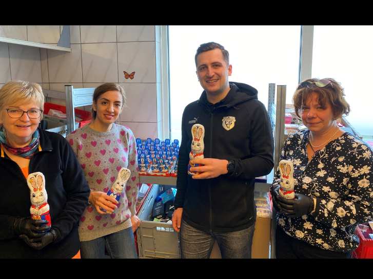 Drei Frauen und ein Mann stehen in der Ausgabestelle der Tafel Bürstadt. Sie halten jeweils Schokohasen in der Hand.