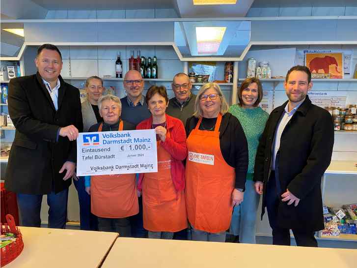 In der Tafelausgabestelle stehen 10 Personen vor einem Lebensmittelregal. 2 Frauen halten das große Plakat der Volksbank in die Höhe, auf der die Spendensumme von 1000,- Euro für die Tafel Bürstadt vermerkt ist.