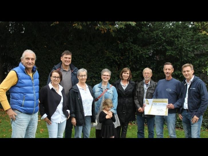 Auf einer Rasenfläche vor einem Wald stehen 8 Erwachsene und ein Kind. Zwei Männer halten den Check für die Tafel Lampertheim und die Tafel Bürstadt in den Händen