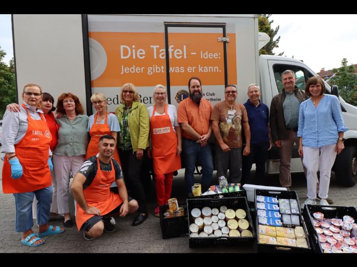 Mitarbeitende der Tafel Lampertheim und Spender stehen gemeinsam vor dem Bus der Tafel Lampertheim. Im Vordergrund sind die Lebensmittel in schwarzen Körben abgebildet.