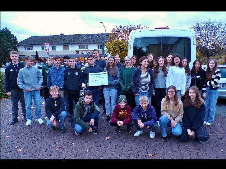 Die Konfirmanden der evangelischen Kirche Rimbach halten den Scheck über 1120 Euro hoch, den sie für die Tafel Rimbach gesammelt haben. Sie Stehen vor einem Bus der Tafel Rimbach auf dem Hof des Psychosozialen Zentrums der Regionalen Diakonie Bergstraße