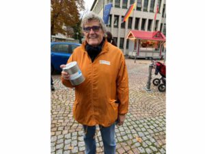 Mann mit orangefarbener Jacke und Spendenbüchse steht auf dem Martinsmarkt in Fürth