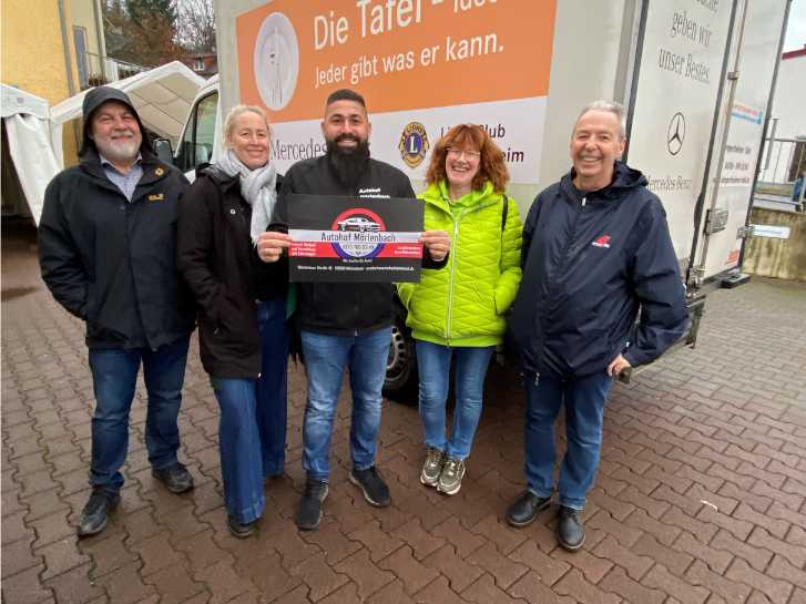 Auf dem Hof der Tafelausgabestelle in Rimbach stehen vor dem Tafel-Auto 5 Personen. Drei Männer und zwei Frauen. Der Mann in der Mitte hält ein Plakat hoch, auf dem das Logo des Autohofs Mörlenbach und die Spendensumme für die Tafel Rimbach abgedruckt sind.