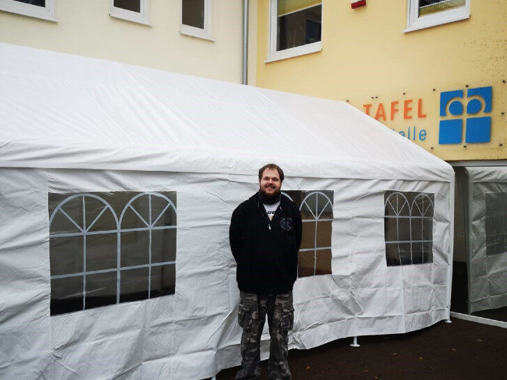 Maximilian Zeller steht vor dem von ihm gespendeten Zelt. Im Hintergrund ist das Gebäude der Tafelausgabestelle Rimbach zu sehen.