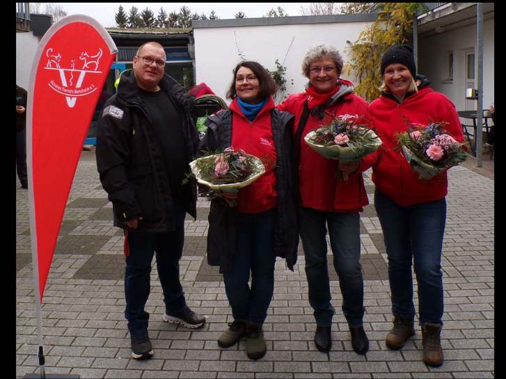 Im Hof des Zentrums für Wohnungslosenhilfe stehen neben einer Beachflag, mit dem Logo " soziales Tiernetz Bensheim e.V." stehen ein Mann und drei Frauen. Die Frauen halten je einen Blumenstrauß in der Hand. Diese hatte Björn Metzgen, Leiter des ZDW Bensheim ihnen überreicht