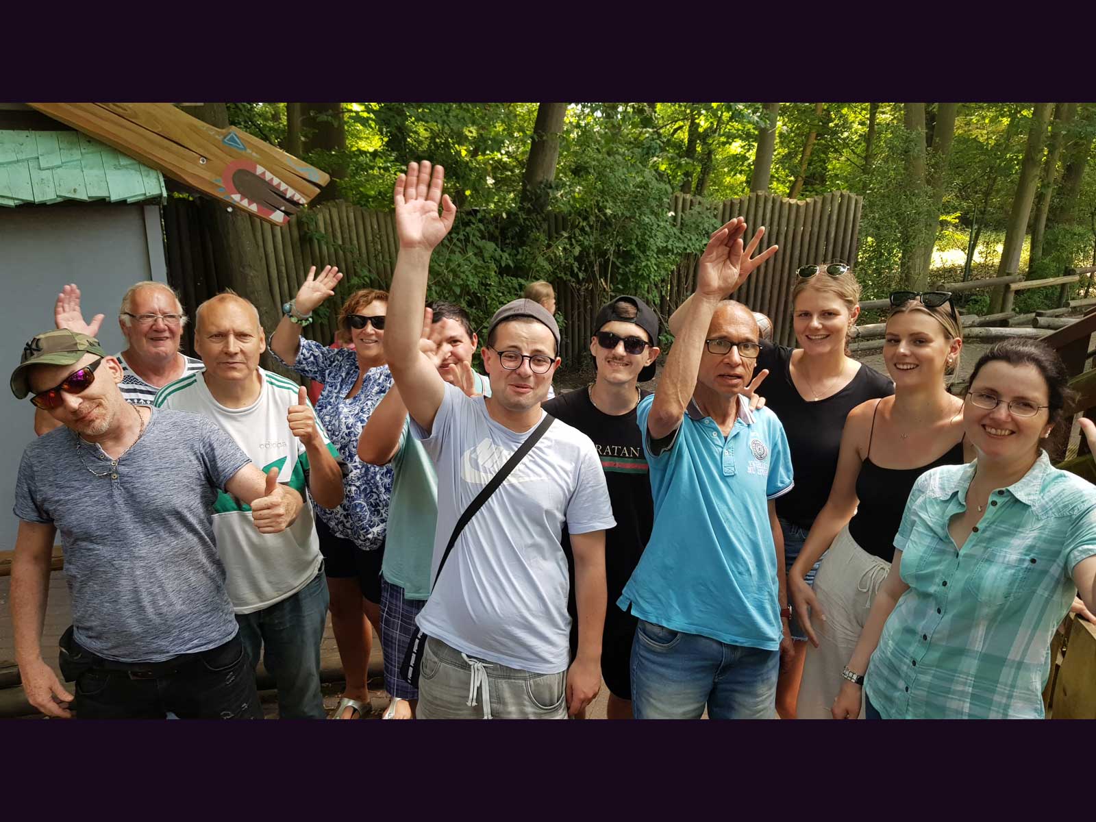 Eine Gruppe Menschen steht im Freizeitpark und winkt fröhlich in die Kamera.