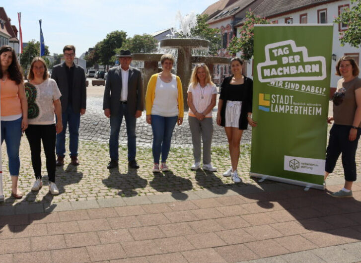 Acht Organisatoren des Tags der Nachbarn stehen mit einem Roll Up nebeneinander