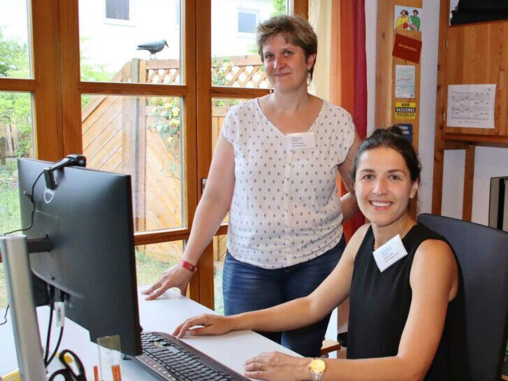 Auf einem Bürostuhl sitzt Samira Osti. Dahinter steht Kerstin Biehal. Das Bild zeigt das Quartiersbüro der Gemeinwesenarbeit in Lampertheim.