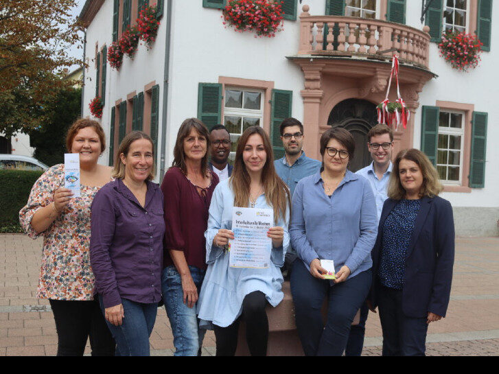 Sechs Frauen in vorderer Reihe und drei Männer dahinter schauen in die Kamera. Zwei Personen zeigen Flyer und Aushänge für die Interkulturelle Woche der Stadt Lampertheim