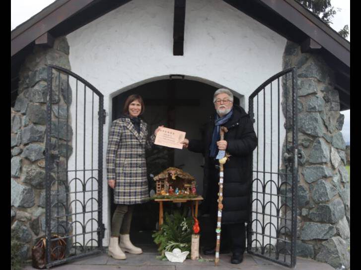 Der Spender und die Tafelkoordinatorin stehen vor der Kapelle und halten den Scheck in die Höhe