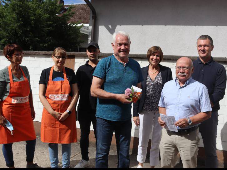 Mitarbeiter:innen der Tafel stehen nach Überreichung des Gutscheins vor einem Gebäude