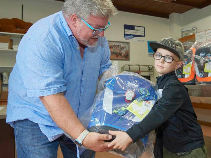 Auf dem Foto übergibt ein Mann einen Schulranzen an ein Kind. © Berno Nix