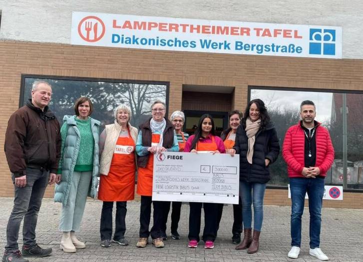 Vor dem Gebäude der Tafel Lampertheim stehen 9 Personen und präsentieren den übergebenen Scheck