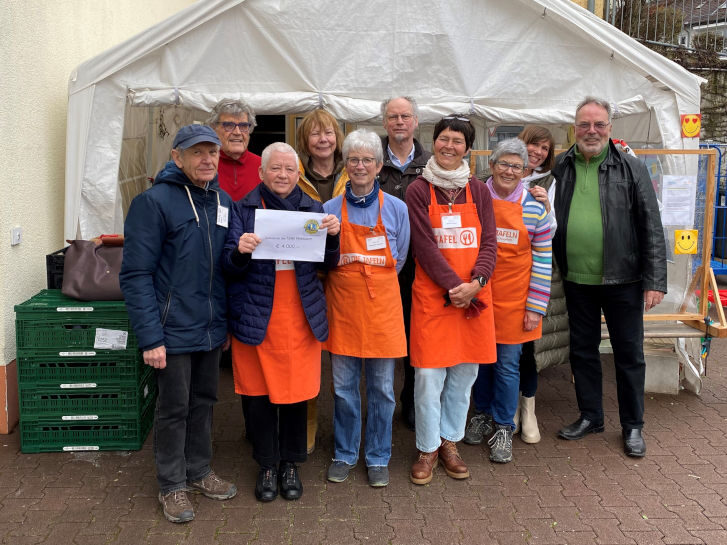 Tafelmitarbeitende stehen vor einem Pavillon und halten einen Spendenscheck hoch.